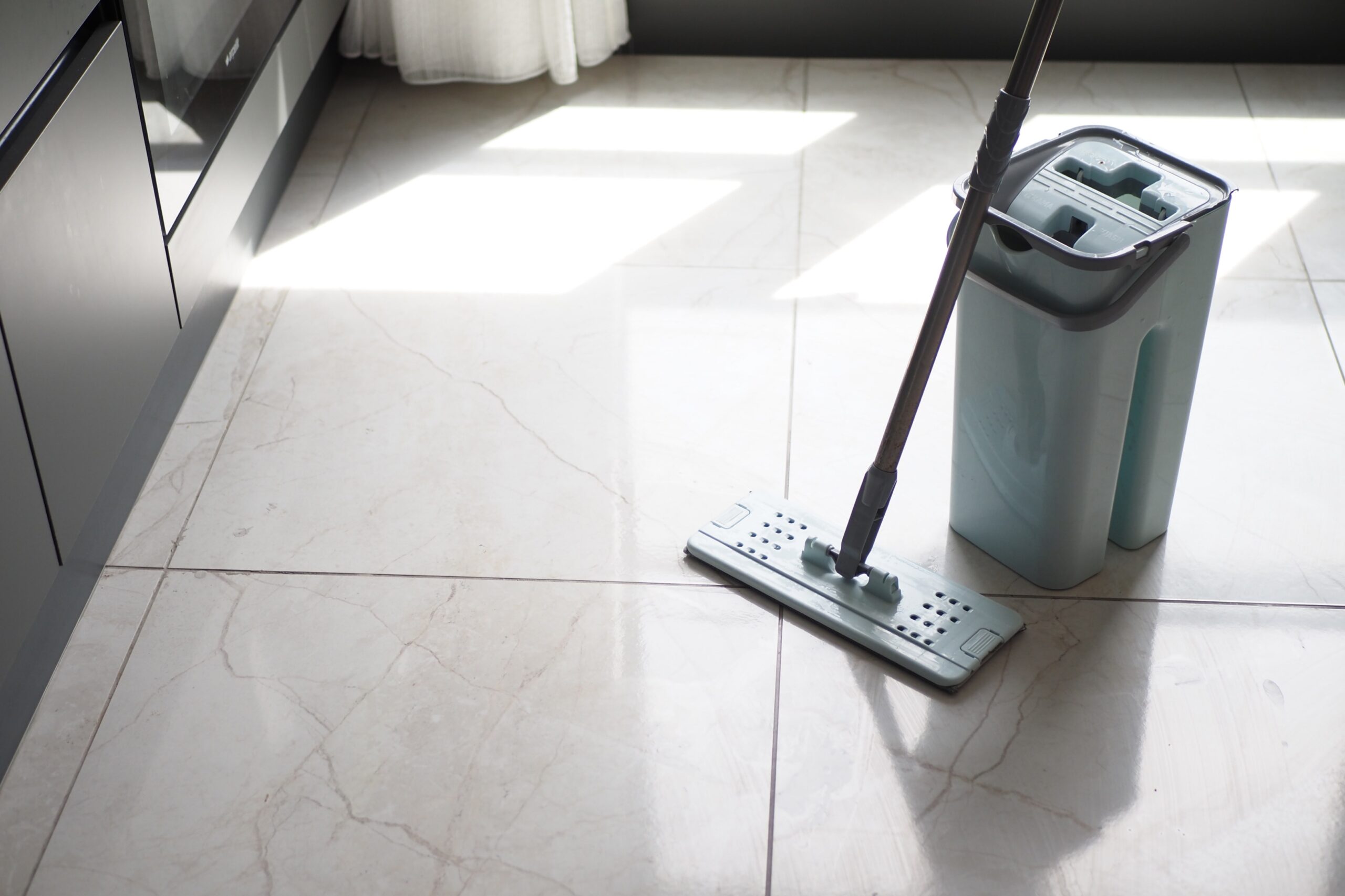Mopping ceramic floor tiles with a flat mop and water bucket to keep tiles clean and shiny