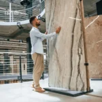Man inspecting a large natural stone slab at a showroom, highlighting granite’s unique texture and durability