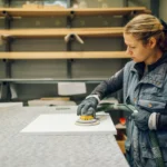 female fabricator sanding stone countertop template with electric sander