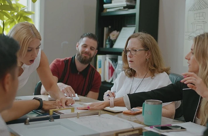 Five people discussing cabinet door samples and hardware around wooden table in office