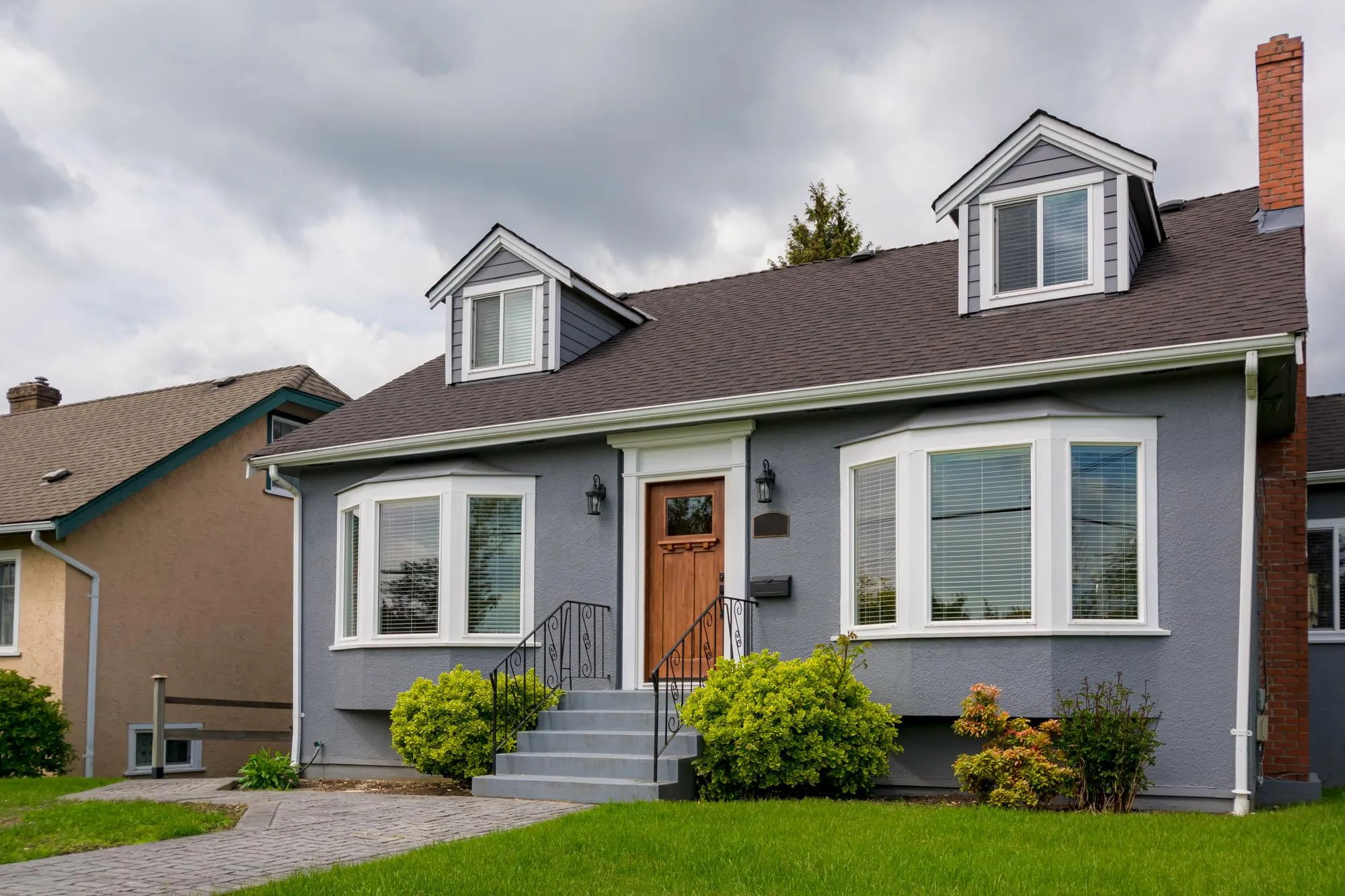 Gray bungalow house exterior with white trim, dormers, and front yard