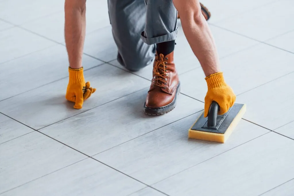 Worker cleaning porcelain tile joints with sponge tool for proper tile maintenance