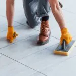 Worker cleaning porcelain tile joints with sponge tool for proper tile maintenance